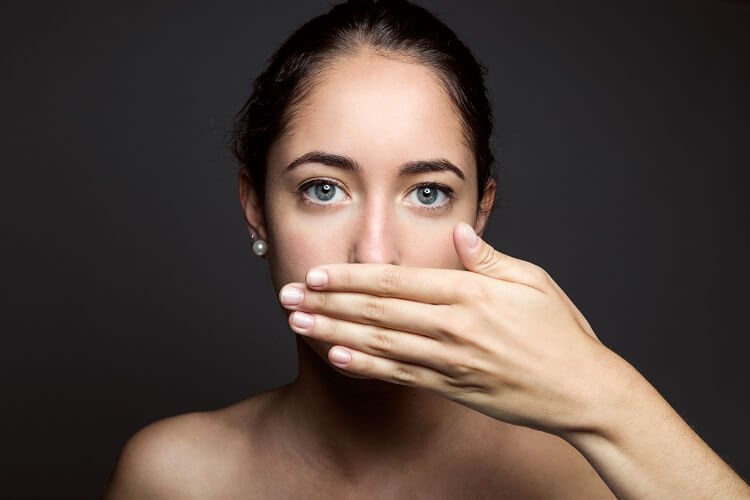 A woman is covering her mouth due to having bad breath.