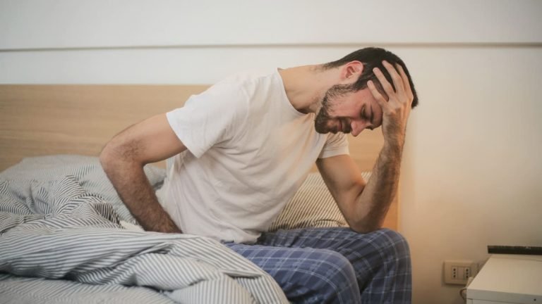 A man in a hangover state holding his hand after drinking lots of alcohol.