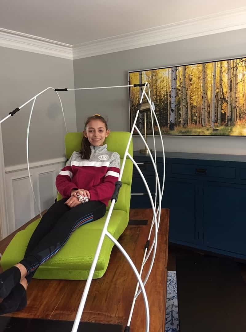 A girl is laying inside a hyperbaric oxygen therapy chamber reading a book