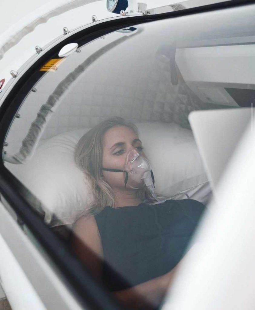 A woman is laying comfortably inside the Hard Shell Hyperbaric Oxygen Chamber 34"D