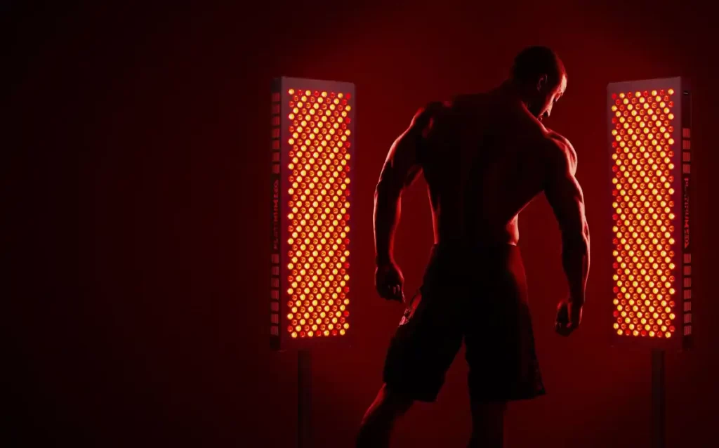 A muscled man standing in front of two red light emitting panels