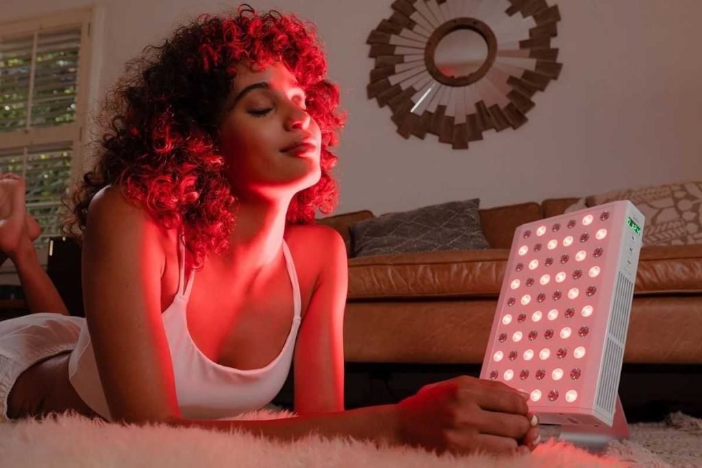 A woman is laying next to a red light emitting device