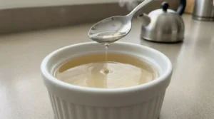 Fully melted gelatin in a white ramekin showing a completely clear, runny liquid consistency after adding boiling water.