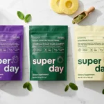 Three Xtend-Life SuperDay powder pouches for Adults, Kids, and 60+ displayed on a marble countertop with a mixed green drink, mint leaves, and pineapple slices