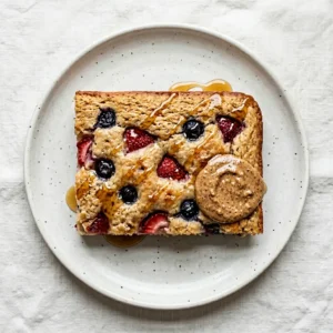 Single slice of baked sheet pan pancake on white plate with maple syrup and almond butter topping